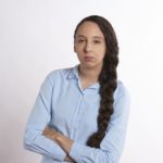 Woman in blue shirt with arms crossed looking determined.