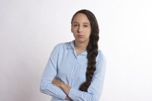 Woman in blue shirt with arms crossed looking determined.