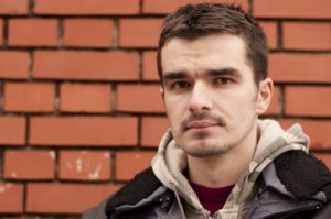 Young man looking at camera with serious face and brick wall background.