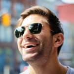 Man wearing sunglasses, looking up and smiling.