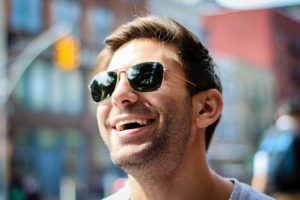 Man wearing sunglasses, looking up and smiling.