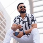 Young, bearded South Asian man with sunglasses sitting in the city outdoors.