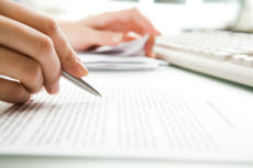 Close-up of hand holding pen reviewing documents.