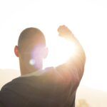 Silhouette of man with hand raised twoard sunlight.