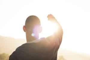 Silhouette of man with hand raised twoard sunlight.